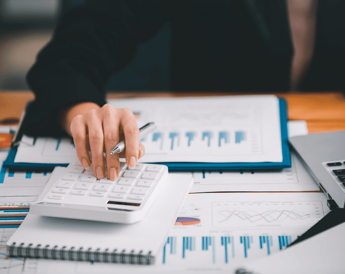 Person using calculator with financial charts.