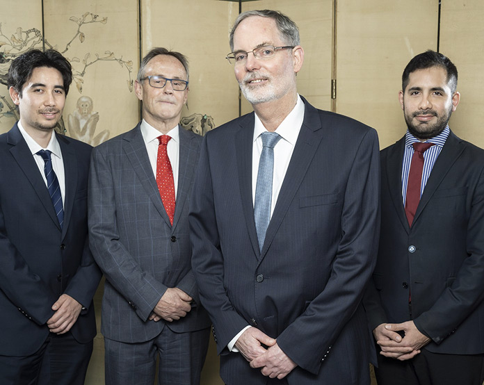 Four businessmen in suits standing together indoors.
